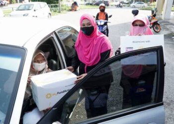 NORIAH Yahya menyerahkan sumbangan kotak makanan kepada penerima secara pandu lalu di Ipoh hari ini. - UTUSAN/ASLIZA MUSA