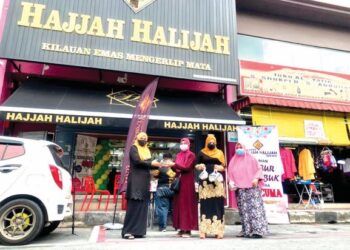 KAKITANGAN kedai emas Hajjah Halijah, Syakila Hussein (kiri) dan Myrah Mustaffa (kanan) mengedarkan bubur lambuk percuma kepada orang ramai di hadapan kedai emas tersebut di Kangar, Perlis. – UTUSAN/MOHD. HAFIZ ABD. MUTALIB