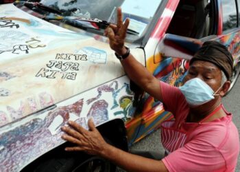 Abdul Rahman Abu Bakar, mengelap kereta Proton Saga miliknya yang dihiasi dengan mesej kesedaran Covid-19 ketika ditemui di Taman Cempaka, Sungai Rambai, Jasin.