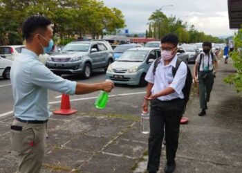 Guru KKHS menyembur cecair penbasmi kuman pada tangan pelajar sebelum memasuki kawasan sekolah. UTUSAN/ SURAIDAH ROSLAN