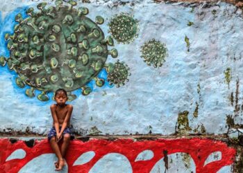 SEORANG budak lelaki duduk di hadapan mural Covid-19 di Bogor, Jawa Barat, Indonesia. - AFP